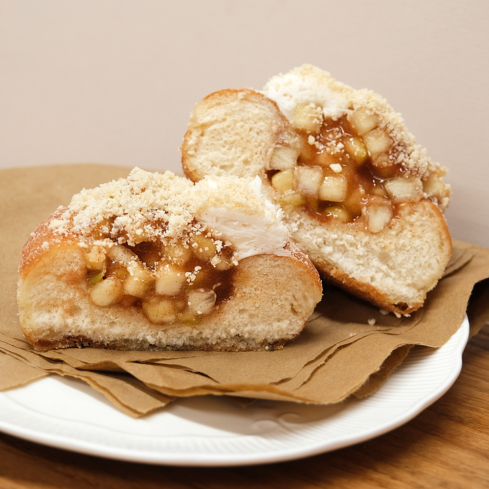 An apple & cinnamon doughnut sliced through the middle so you can see the apple spilling out