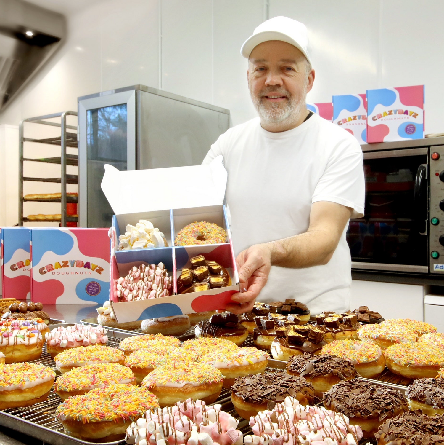 Business owner Neil in the bakery surrounded by doughnuts of varying flavours