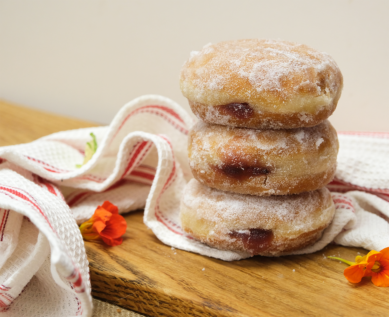 A tower of jam doughnuts covered in sugar with orange flowers 